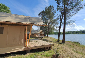 Tentes safari en bord de lac sous un ciel bleu à Huttopia Lac de l'Uby - Gers, France.