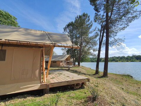 Tentes safari en bord de lac sous un ciel bleu à Huttopia Lac de l'Uby - Gers, France.