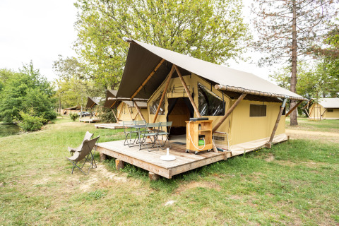 Safari Trappeur tent with wooden deck, outdoor seating, and trees in a peaceful green camping area.