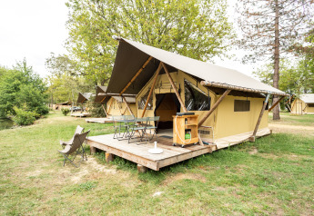 Safari-Trappeur-Zelt auf einer hölzernen Terrasse, umgeben von Bäumen und Rasen auf einem Campingplatz.