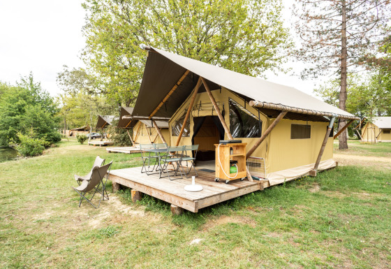 Safari-Trappeur-Zelt auf einer hölzernen Terrasse, umgeben von Bäumen und Rasen auf einem Campingplatz.