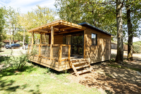 Houten huisje genaamd Chalet Evasion met veranda, omgeven door bomen en natuur op een zonnige dag.