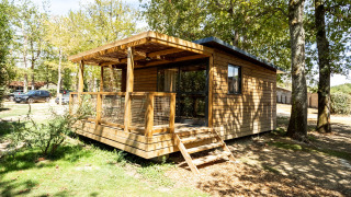 Cabaña de madera llamada Chalet Evasion con porche, rodeada de árboles y naturaleza en un día soleado.