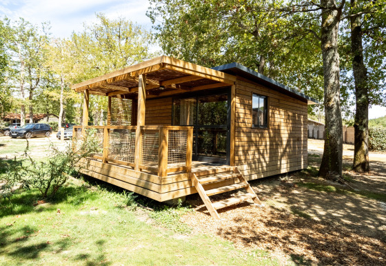 Houten chalet Chalet Evasion met veranda, omgeven door bomen en natuur op een zonnige dag.