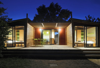 Moderne vakantiewoning met grote glaspartijen en terras 's avonds bij Camping d'Angers - Lac de Maine, Frankrijk.