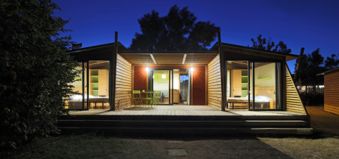 Moderne vakantiewoning met grote glazen deuren en terras 's avonds bij Camping d'Angers - Lac de Maine, Frankrijk.