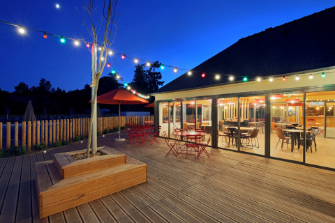 Terrazza all'aperto con luci e tavoli colorati di sera al Camping d'Angers - Lac de Maine in Francia.