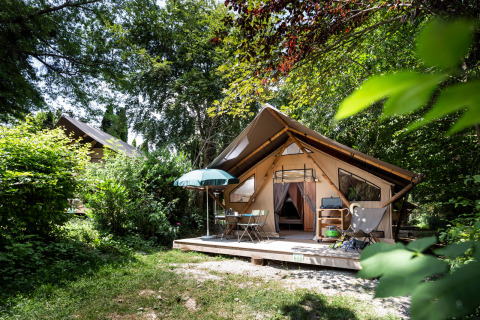 Glamping tent met houten terras en tuinmeubilair in een groene, bosrijke omgeving van het vakantiepark.
