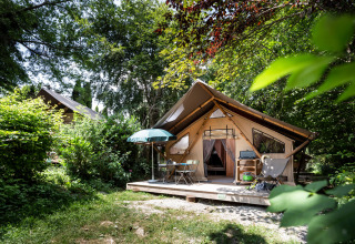 Tenda glamping con veranda e arredi da esterno in un parco vacanze verde circondato da alberi.