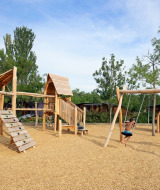 Parque infantil de madera con columpios en Camping d'Angers - Lac de Maine, niños juegan bajo el sol.