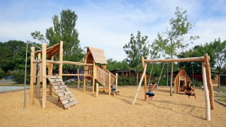 Parque infantil de madera con columpios en Camping d'Angers - Lac de Maine, niños juegan bajo el sol.