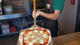 Un pizzero sonriente en Camping d'Angers - Lac de Maine sirve una pizza recién horneada a los huéspedes.