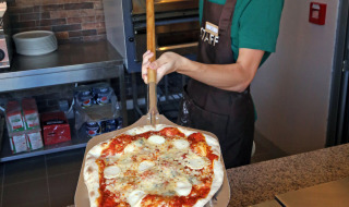 Un pizzero sonriente en Camping d'Angers - Lac de Maine sirve una pizza recién horneada a los huéspedes.