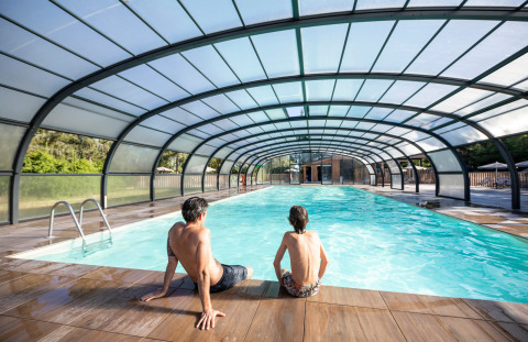 Dos personas están sentadas junto a una piscina cubierta en Village Huttopia Lac de Rillé, Centre-Val de Loire, Francia.