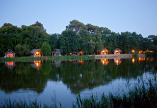 Avondzicht op verlichte hutten aan het meer in Village Huttopia Lac de Rillé, Centre-Val de Loire, Frankrijk.