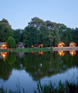 Vista nocturna de cabañas iluminadas junto al lago en Village Huttopia Lac de Rillé, Centre-Val de Loire, Francia.