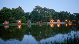 Vista nocturna de cabañas iluminadas junto al lago en Village Huttopia Lac de Rillé, Centre-Val de Loire, Francia.