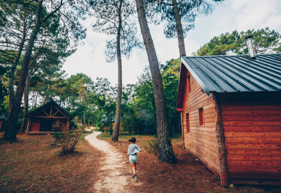 Een kind loopt op een bospad tussen houten hutten in Huttopia Lac de Rillé, Centre-Val de Loire, Frankrijk.