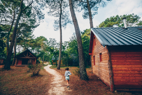 Un bambino corre su un sentiero tra le cabine di legno al villaggio Huttopia Lac de Rillé, Centre-Val de Loire.