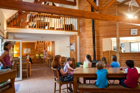Kinderen en volwassenen genieten van de gemeenschappelijke ruimte in een houten chalet bij Huttopia Lac de Rillé, Frankrijk.