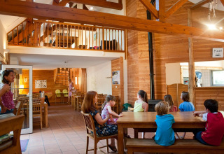 Enfants et adultes profitent de l’espace commun d’un chalet en bois au Village Huttopia Lac de Rillé, France.