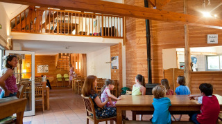 Niños y adultos disfrutan del área común de una acogedora cabaña en Village Huttopia Lac de Rillé, Francia.