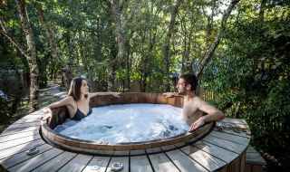 Dos personas se relajan en un jacuzzi al aire libre rodeado de árboles en Village Huttopia Lac de Rillé, Francia.