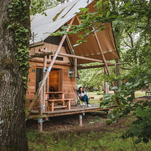 Mujer relajándose en el porche de una cabaña de madera en el bosque en Village Huttopia Lac de Rillé, Francia.