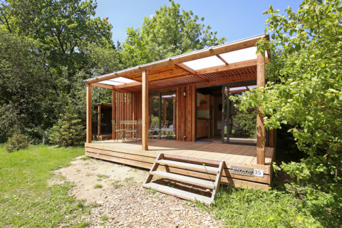 Træhytte med terrasse ved Camping de Lyon i Auvergne-Rhône-Alpes, Frankrig, omgivet af grøn natur.