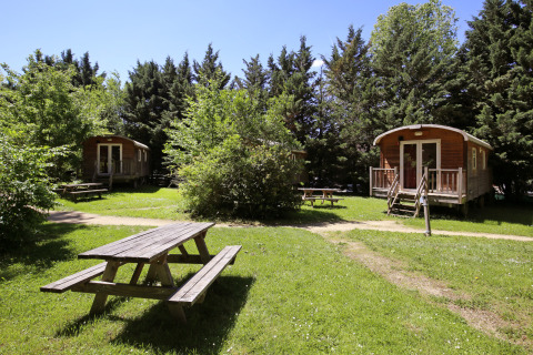Houten huisjes en picknickbanken in een groene omgeving op Camping de Lyon, Auvergne-Rhône-Alpes, Frankrijk.