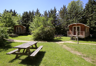 Houten huisjes en picknickbanken in een groene omgeving op Camping de Lyon, Auvergne-Rhône-Alpes, Frankrijk.