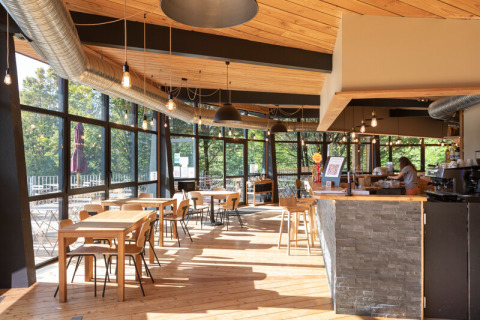 Cafetería luminosa y moderna en Camping de Lyon, Auvergne-Rhône-Alpes, con ventanas grandes y decoración de madera.