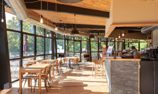 Cafetería luminosa y moderna en Camping de Lyon, Auvergne-Rhône-Alpes, con ventanas grandes y decoración de madera.