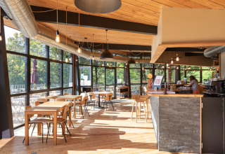 Cafetería luminosa y moderna en Camping de Lyon, Auvergne-Rhône-Alpes, con ventanas grandes y decoración de madera.