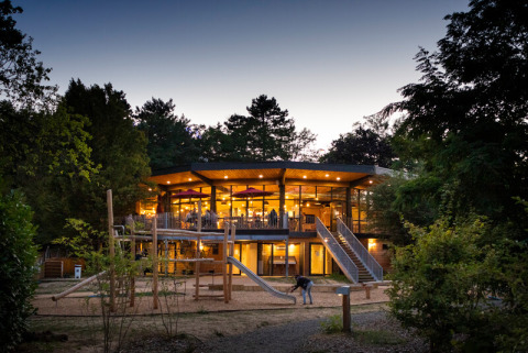 Avondbeeld van een modern, verlicht gebouw met speeltuin op Camping de Lyon in Auvergne-Rhône-Alpes, Frankrijk.