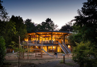 Avondbeeld van een modern, verlicht gebouw met speeltuin op Camping de Lyon in Auvergne-Rhône-Alpes, Frankrijk.