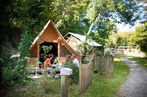 Family sitting outside a tent at Camping de Lyon holiday park in Auvergne-Rhône-Alpes, France, in nature.