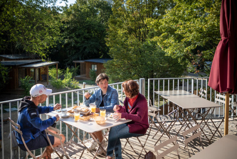 Drie personen genieten van hun ontbijt op een terras tussen het groen in Camping de Lyon, Auvergne-Rhône-Alpes.