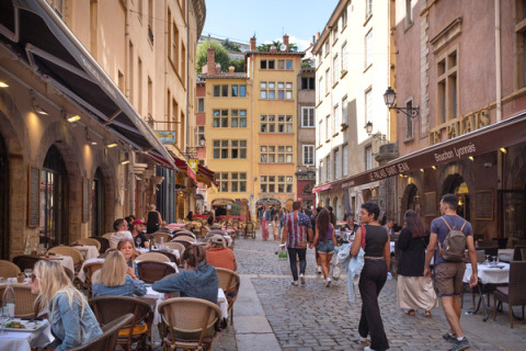 Personas comiendo en terrazas y paseando por una calle adoquinada en Dardilly, Auvergne-Rhône-Alpes, Francia.
