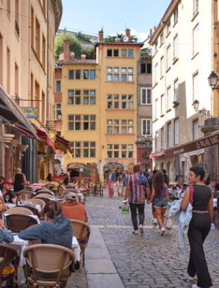 Personas comiendo en terrazas y paseando por una calle adoquinada en Dardilly, Auvergne-Rhône-Alpes, Francia.