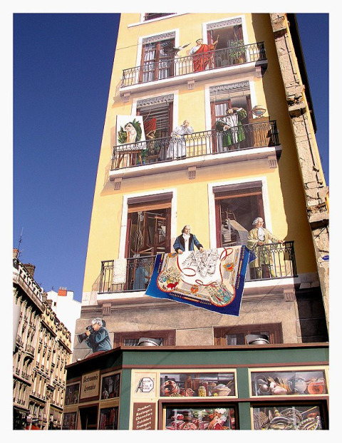 Un mural colorido en un edificio de Lyon, Francia, muestra personas en balcones y ventanas.