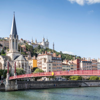 Vista de un puente rojo, una iglesia y edificios coloridos junto al río en Lyon, Francia, en un día soleado.