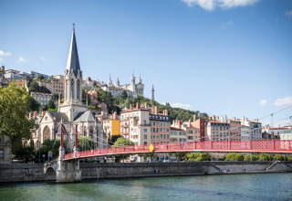 Vista de un puente rojo, una iglesia y edificios coloridos junto al río en Lyon, Francia, en un día soleado.