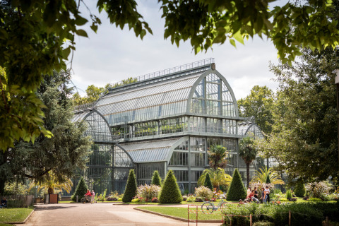 Large glass greenhouse with lush gardens and people at Camping de Lyon, Auvergne-Rhône-Alpes, France, on a sunny day.
