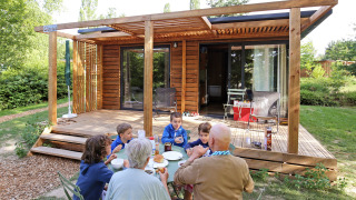 Familia desayunando afuera de una cabaña de madera en Chalet Ottawa, rodeada de vegetación.