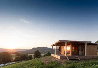 Træhytte Chalet Evasion Vista på en bakkeskråning ved solnedgang med udsigt over dalen og bjergene.