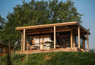 En træhytte med overdækket terrasse omgivet af grønne træer ved Chalet Evasion Vista, Huttopia Pays de Cordes sur Ciel.
