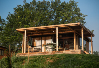 Cabaña de madera con porche en Chalet Evasion Vista de Huttopia Pays de Cordes sur Ciel en Francia, rodeada de árboles.