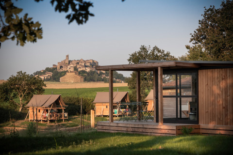 Holzhütten und Safarizelte im Huttopia Pays de Cordes sur Ciel, mit Blick auf Cordes sur Ciel im Hintergrund.