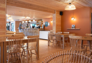 Træbeklædt caféinteriør med borde og stole på Huttopia Pays de Cordes sur Ciel i Occitanie, Frankrig.